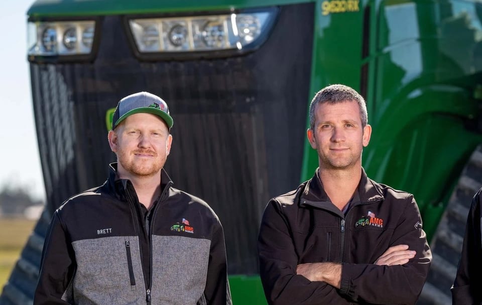 Two AMC Farms team members standing in front of a tracked tractor in Brawley, California.